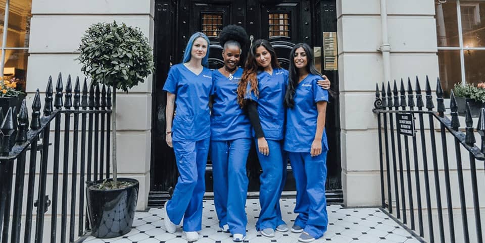 Four nurses in blue scrubs outside a Georgian clinic entrance, EMfusion skin longevity treatment London